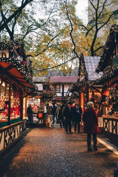 people are walking through an outdoor market with christmas decorations on the walls and trees in the background