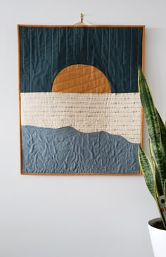 a potted plant sitting next to a wall hanging on a wall with a quilt