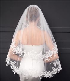 the back of a bride's veil with white flowers and leaves on it, against a black background