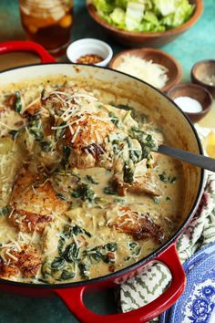 a red pot filled with chicken and spinach covered in grated parmesan cheese