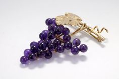 "The 14kt. gold One Leaf and Vine Brooch has a large leaf and a gold runner wire on an 1 1/8\" long vine. The grape cluster has 29 4mm. round natural dark Amethyst gemstones hand mounted to a 14kt. gold grape stem. That is over 3 1/2 carats total weight of Amethyst gemstones! The Cabernet Leaf has a lot of engraved detail as well as engraved detail on the grape stem. The pin on the back is a hinged pin stem with a joint and catch. Overall actual size of this piece is 1 1/2\" tall by 1 1/8\" wide Amethyst Brooch Jewelry Gift, Purple Brooch Jewelry Gift, Elegant Purple Brooches For Anniversary, Elegant Gold Amethyst Brooches, Amethyst Brooch For Anniversary, Amethyst Brooch Jewelry For Anniversary, Elegant Grape Colored Jewelry For Gift, Gold Runner, Dark Amethyst