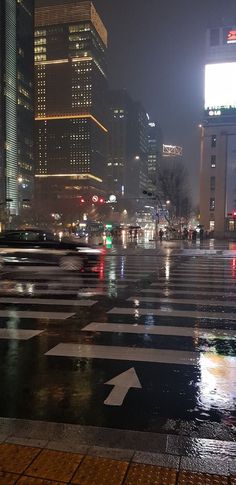 a city street at night with cars driving on the road and buildings in the background