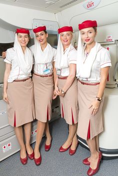 the cabin attendants are all dressed in red hats and tan skirts, posing for a photo