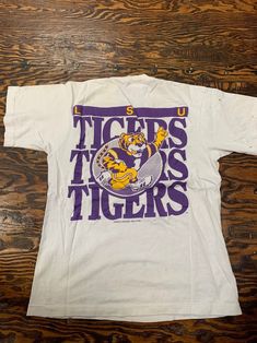 a white t - shirt with the lsu tigers on it sitting on a wooden floor