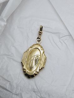 This is a very unique pendant---the shape is not often seen.  The geometric details at the edges really bring out the Art Deco style. The locket is quite large, at a little less than two inches long by 1 1/4 inch wide.  The total drop length with the clip is nearly three inches. The front of the locket has a hand carved floral design with a blank area for a monogram.  The back is polished gold-tone. The inside of the locket is clean and ready for portraits. I have included the clip so you can easily add the locket to your favorite chain. This piece is in excellent condition.   Free shipping in USA. Vintage Medallion Jewelry With Detachable Pendant, Heirloom Pendant Locket Necklace With Charms, Vintage Yellow Gold Jewelry With Detachable Pendant, Unique Engraved Gold Locket Necklace, Ornate Pendant Locket Necklace Collectible, Collectible Ornate Pendant Locket Necklace, Ornate Pendant Locket Necklace For Collectors, Art Deco Medallion Locket Jewelry, Collectible Heirloom Jewelry With Large Pendant