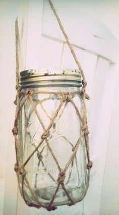 a glass jar with rope wrapped around it on top of a wooden table next to a white wall