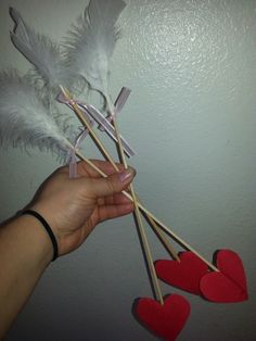 someone is holding three heart - shaped sticks with white feathers and red hearts on them