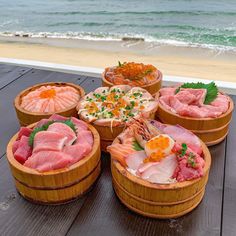 several wooden bowls filled with different types of food on a table near the ocean and beach