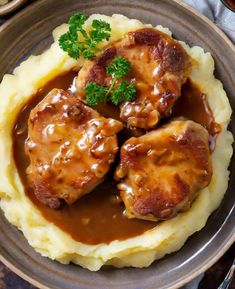 three pieces of meat covered in gravy on top of mashed potatoes