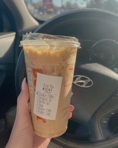 a person holding up a cup of coffee in their hand while sitting in a car