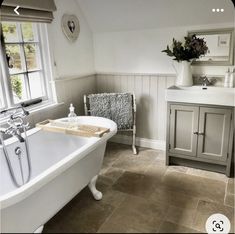 a white bath tub sitting under a window next to a sink in a room with tile flooring