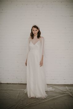 a woman standing in front of a white brick wall wearing a wedding dress and veil