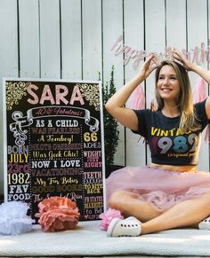 a woman sitting on the ground in front of a chalkboard sign and pink tutu skirt