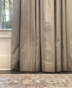 a cat sitting on top of a rug in front of a window with drapes