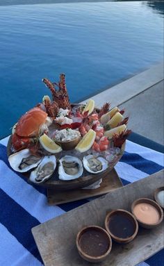 a platter of seafood and dipping sauces on a table next to the water