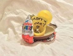 an egg shell with some candy in it on a white sheeted surface and the words marry me written on it