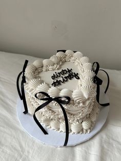 a white cake with black ribbon and happy birthday written on the top is sitting on a bed