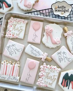 some decorated cookies are in a tray on top of a table with pink and white decorations