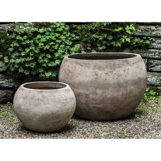 two large pots sitting next to each other in front of a stone wall and shrubbery