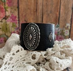 a black leather cuff bracelet with an intricate design on the front and center, sitting on top of a white crocheted blanket