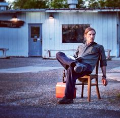 a man sitting on top of a wooden chair in front of a building with a suitcase