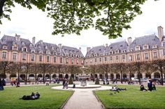 people are sitting on the grass in front of a building with many windows and trees