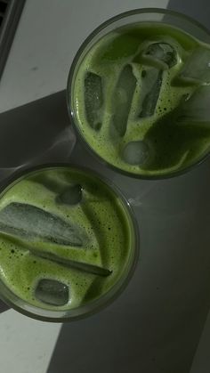 two glasses filled with green liquid sitting on top of a white counter next to each other