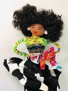 a doll with an afro is sitting on a black and white striped skirt, wearing a colorful dress