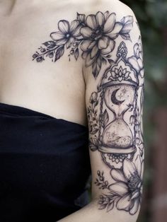 a woman wearing a black dress with flowers and an hour glass tattoo on her arm