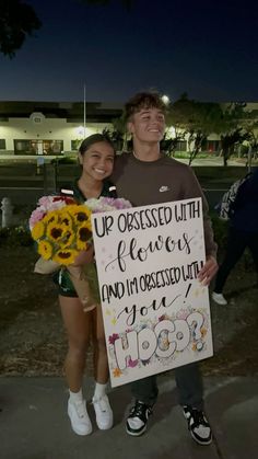 a man and woman standing next to each other holding a sign that says up dressed with flowers and i'm interested in you too