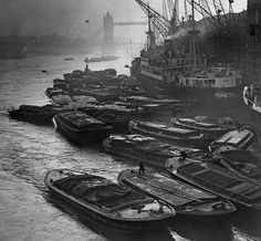 many boats are docked in the water near a bridge and tower cranes on a foggy day