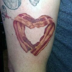 a heart shaped bacon tattoo on the left arm with two birds flying above it and an orange ribbon in the shape of a heart