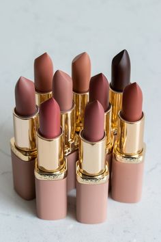 several lipsticks are lined up in a row on a white surface, one is pink and the other is brown