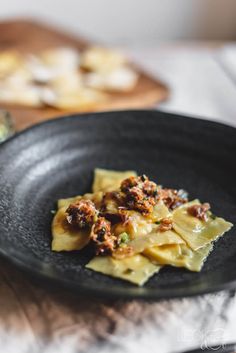 a black plate topped with pasta and meat on top of a wooden cutting board next to other food items