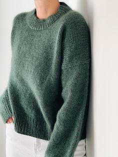 a woman wearing a green sweater leaning against a wall with her hands on her hips