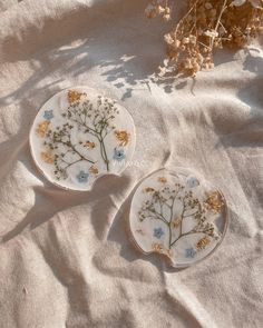 two plates sitting on top of a table covered in white cloth next to dried flowers