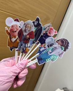 a person in pink gloves holding up stickers with cartoon characters on them and wearing rubber gloves