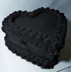 a black heart shaped cake sitting on top of a white tablecloth covered countertop