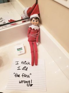 an elf is sitting on the sink next to a note that says i think i did the floss wrong