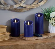 three blue candles sitting on top of a wooden table next to a vase with flowers