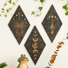 two black and gold wall hangings on a white wall next to potted plants