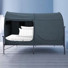 a bed with a cover over it sitting on a wooden floor next to a blue wall