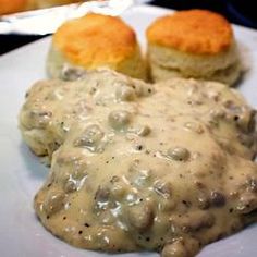 biscuits and gravy on a white plate with two rolls in the background,