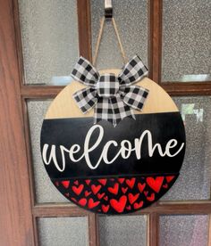 a welcome sign hanging on the front door to someone's house with hearts painted on it