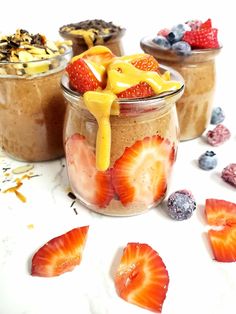 three jars filled with different types of food on top of a white countertop next to strawberries and blueberries