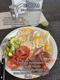 a white plate topped with eggs, tomatoes and avocado next to a glass of water