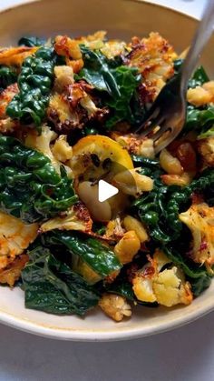 a white plate topped with pasta and spinach covered in seasoning next to a fork