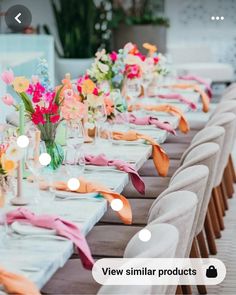 the table is set with white chairs and colorful flowers in vases on each side