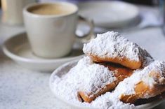 powdered sugar covered donuts on a plate next to a cup of coffee