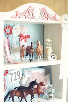 some toy horses are standing on top of a book shelf with numbers and ribbons around them